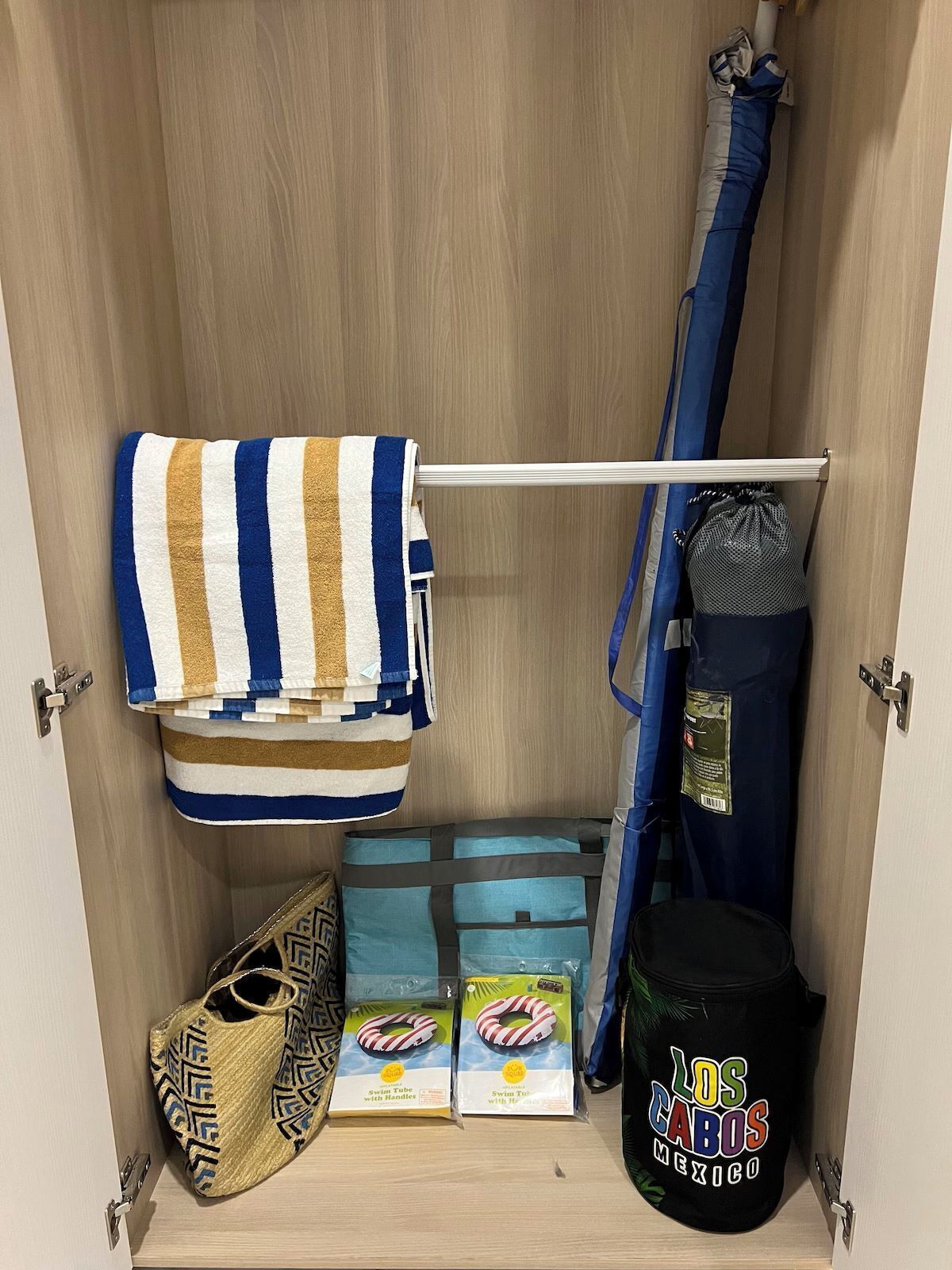 A storage closet with a striped towel, a blue bag, a swim tube with handles, and a black bag with a colorful design.