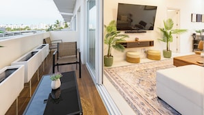 Un salon moderne avec un canapé, une table basse et un téléviseur. On y trouve deux plantes en pot et un tapis sur le sol.