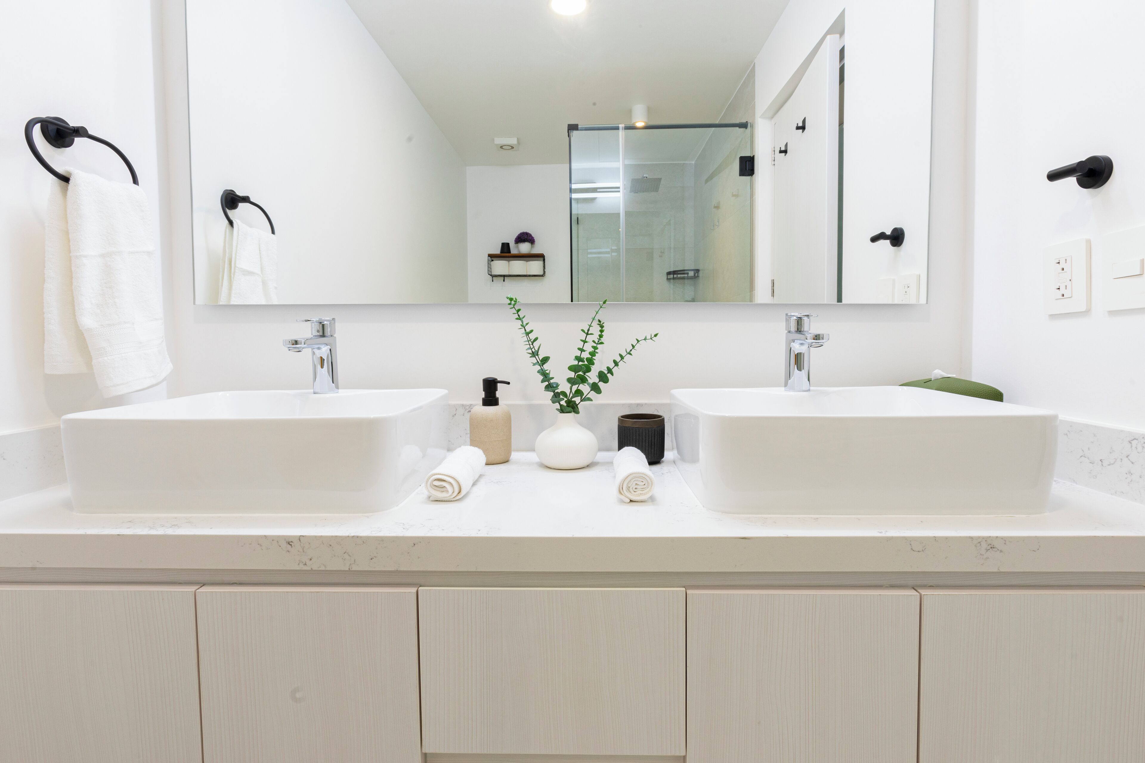 A modern bathroom with two sinks, a large mirror, and a glass shower enclosure.