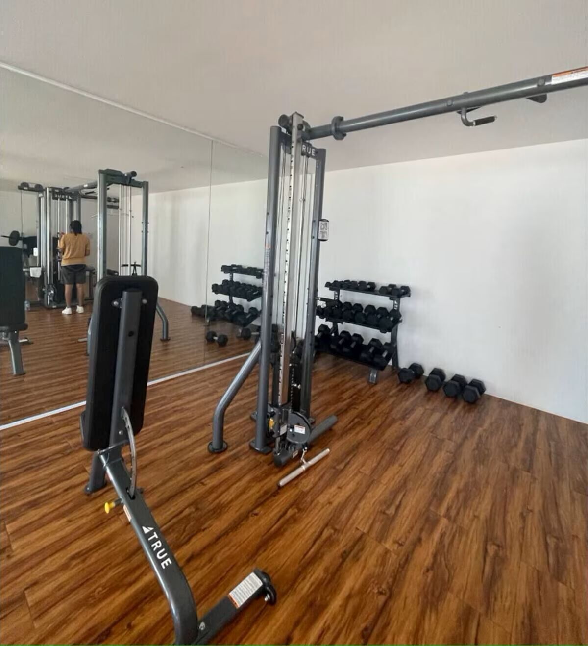 Un gimnasio con equipo de ejercicio, incluyendo una máquina Smith y mancuernas.