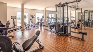 Une salle de sport spacieuse, dotée de divers appareils d’exercice, de grandes fenêtres et d’un plancher en bois.