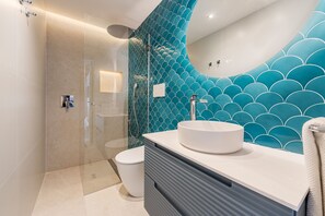 A modern bathroom with a glass shower enclosure, a white sink, and a blue tiled wall. - VILLA ES FIGUERAL (Biniamar)
