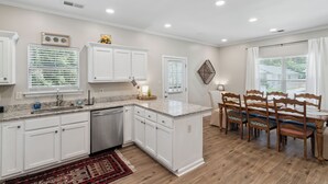 A modern kitchen with white cabinetry, a granite countertop, and a dining area with wooden chairs and a table. - Casa Azul Memphis Midtown Cooper Young (Memphis)
