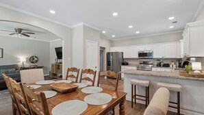 A modern kitchen with white cabinets, stainless steel appliances, and a wooden dining table with placemats. - Casa Azul Memphis Midtown Cooper Young (Memphis)