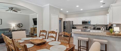 Una cocina moderna con armarios blancos, electrodomésticos de acero inoxidable y una mesa de comedor de madera con individuales.