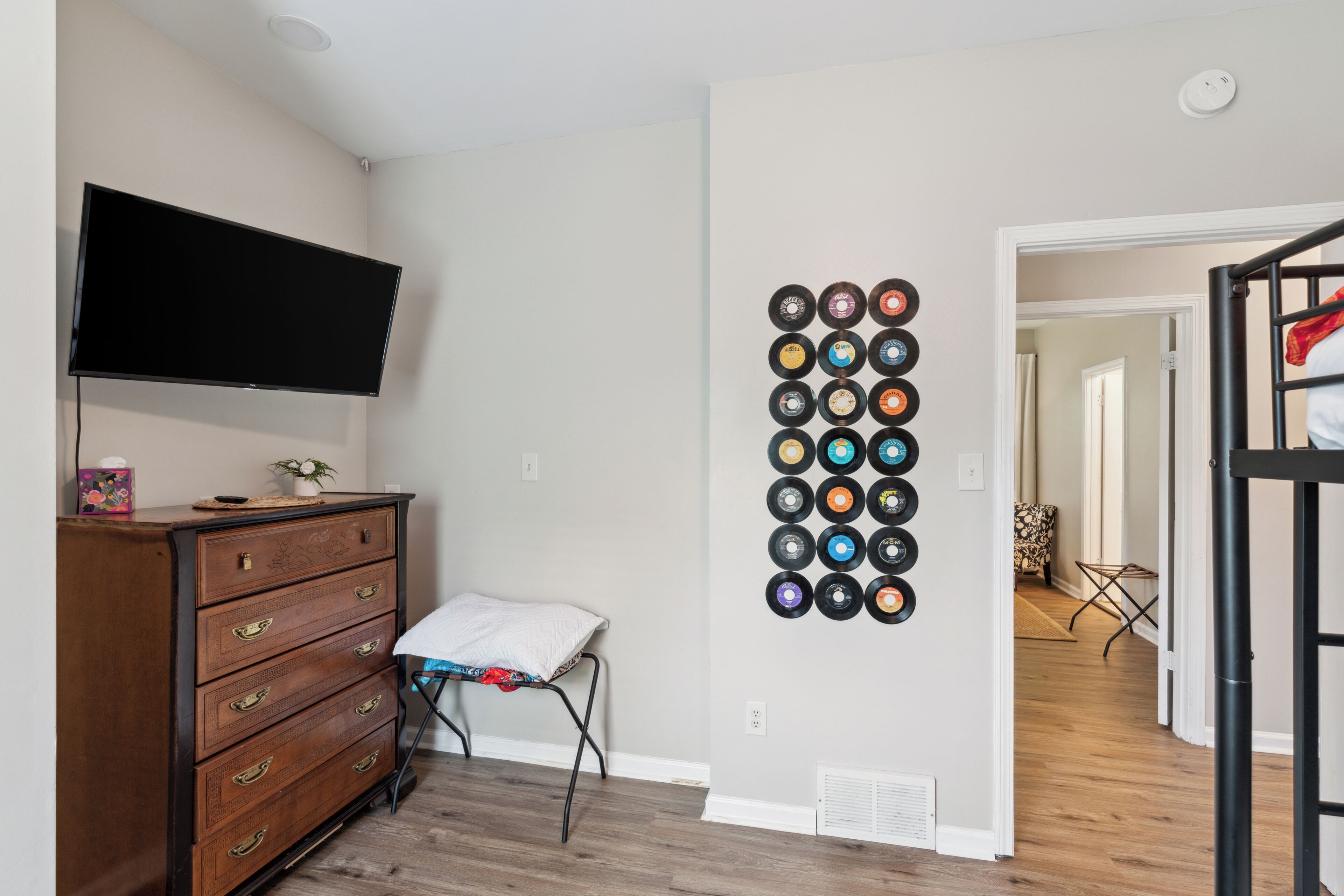 A room with a wooden dresser, a flat-screen TV, a wall-mounted vinyl record collection, and a bunk bed.