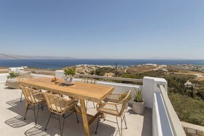 Een houten tafel met rieten stoelen op een balkon met uitzicht op een kustlandschap.