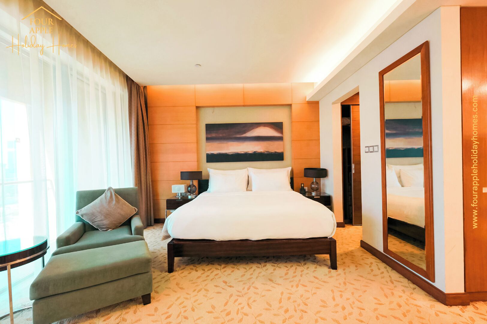 Quarto de hotel com uma cama grande, uma poltrona verde, uma mesa de cabeceira com abajures, um espelho grande e um quadro na parede.