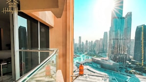 Un balcon doté d’une balustrade en verre, offrant une vue sur un paysage urbain moderne avec de hauts immeubles et une route sinueuse.