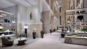 Un hall d’hôtel moderne doté d’un espace salon central, d’un comptoir d’accueil et d’une présentation d’objets décoratifs.