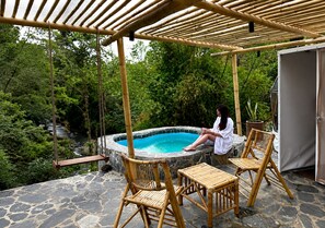 A person relaxing by a stone hot tub under a bamboo pergola, surrounded by lush greenery. - Alma Glamping  (Coatepec)