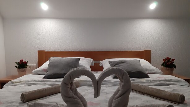 A neatly made bed with towels arranged in a heart shape, a wooden headboard, and two small potted plants on either side. - Charming 2-bedroom apartment 2 with WiFi, AC in delightful Plitvice Lakes (Plitvice lakes)