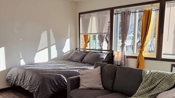 Een slaapkamer met een bed, een bank, een rond tapijt en een raam met gordijnen.