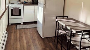 Een compacte keuken met witte kastjes, een fornuis, een koelkast en een eettafel met stoelen.