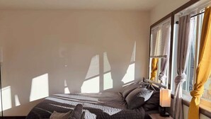 Een slaapkamer met een bed, nachtkastje, lamp en een raam met gordijnen.