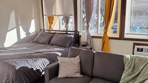 Een slaapkamer met een bed, een grijze bank en een raam met gordijnen.