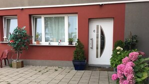 A residential building with a red facade, a white door marked with a 'C', and a small garden area with potted plants and flowers. - Pension Alis (Augsburg)