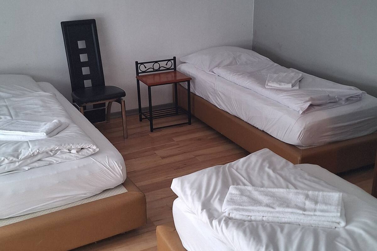 Ein Zimmer mit drei Einzelbetten, einem kleinen Tisch und einem Stuhl.