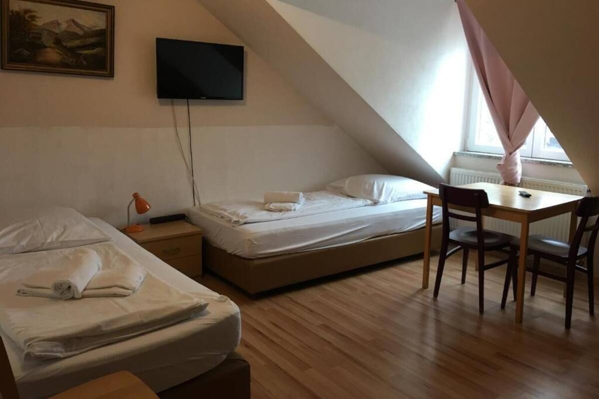 Ein Schlafzimmer mit zwei Betten, einem Schreibtisch, einem Stuhl, einem Fernseher und einem Fenster mit Vorhängen.