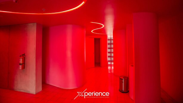 A red-lit hallway with a fire extinguisher, a trash can, and a curved ceiling light. - Secrt Sabana 1BR · Balcony Workspace · City View · Parking · Apt 2915 (Mata Redonda)