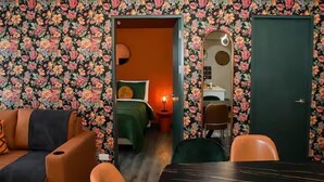 Una habitación con papel tapiz floral, una cama con ropa de cama verde, una mesita y una silla.