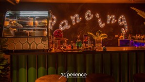 Zona de bar con un letrero de neón que dice "Dancing", un horno bien iluminado y diversos elementos de bar.