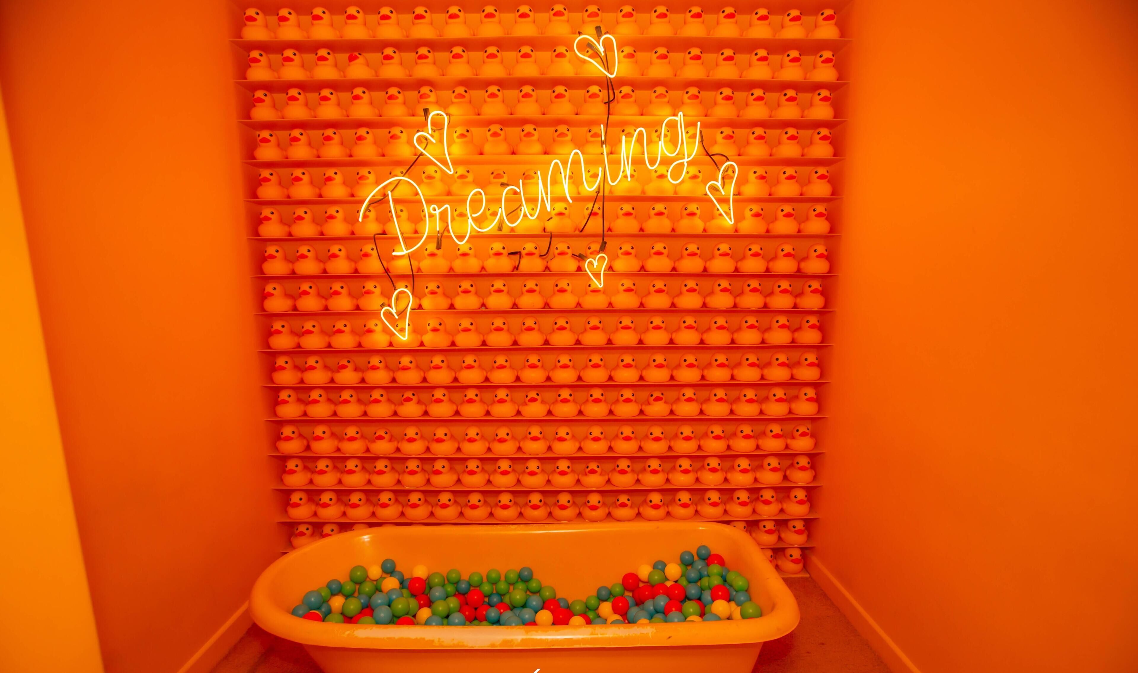 Una habitación con un letrero de neón que dice 'Dreaming' y una bañera llena de bolas de colores.