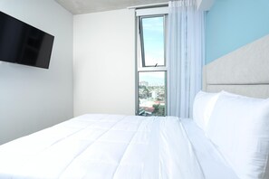 Une chambre d’hôtel avec un lit, un téléviseur fixé au mur et une fenêtre donnant sur des immeubles.