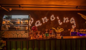Eine Bar mit einem Neonzeichen das „Dancing“ ausschreibt, einem gut beleuchteten Ofen und verschiedenen Barutensilien.