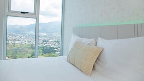 Ein Hotelzimmer mit großem Fenster und Blick auf die Stadt, einem ordentlich bezogenen Bett und einer strukturierten Wand.