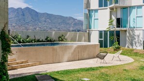 A modern building with a swimming pool, outdoor seating, and a view of mountains.