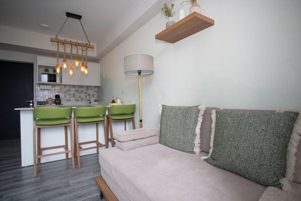 Un salon moderne avec un canapé, une table basse et un coin cuisine équipé de tabourets de bar.