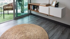 A modern living room with a large TV mounted on the wall, a sliding glass door leading to a balcony, and a wooden bookshelf. - Secrt Sabana 1BR · High Floor · Workspace + WiFi · Parking · Apt 2006 (Mata Redonda)
