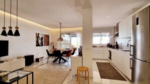 Una cocina moderna con electrodomésticos de acero inoxidable, un comedor con mesa y sillas, y una sala de estar con televisor y una mesita de centro.