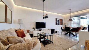 Una sala de estar moderna con sofá, mesa de centro, televisor y comedor.