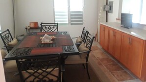 Zona de menjador amb una taula rectangular, sis cadires i una cuina amb armaris de fusta i una superfície de treball.