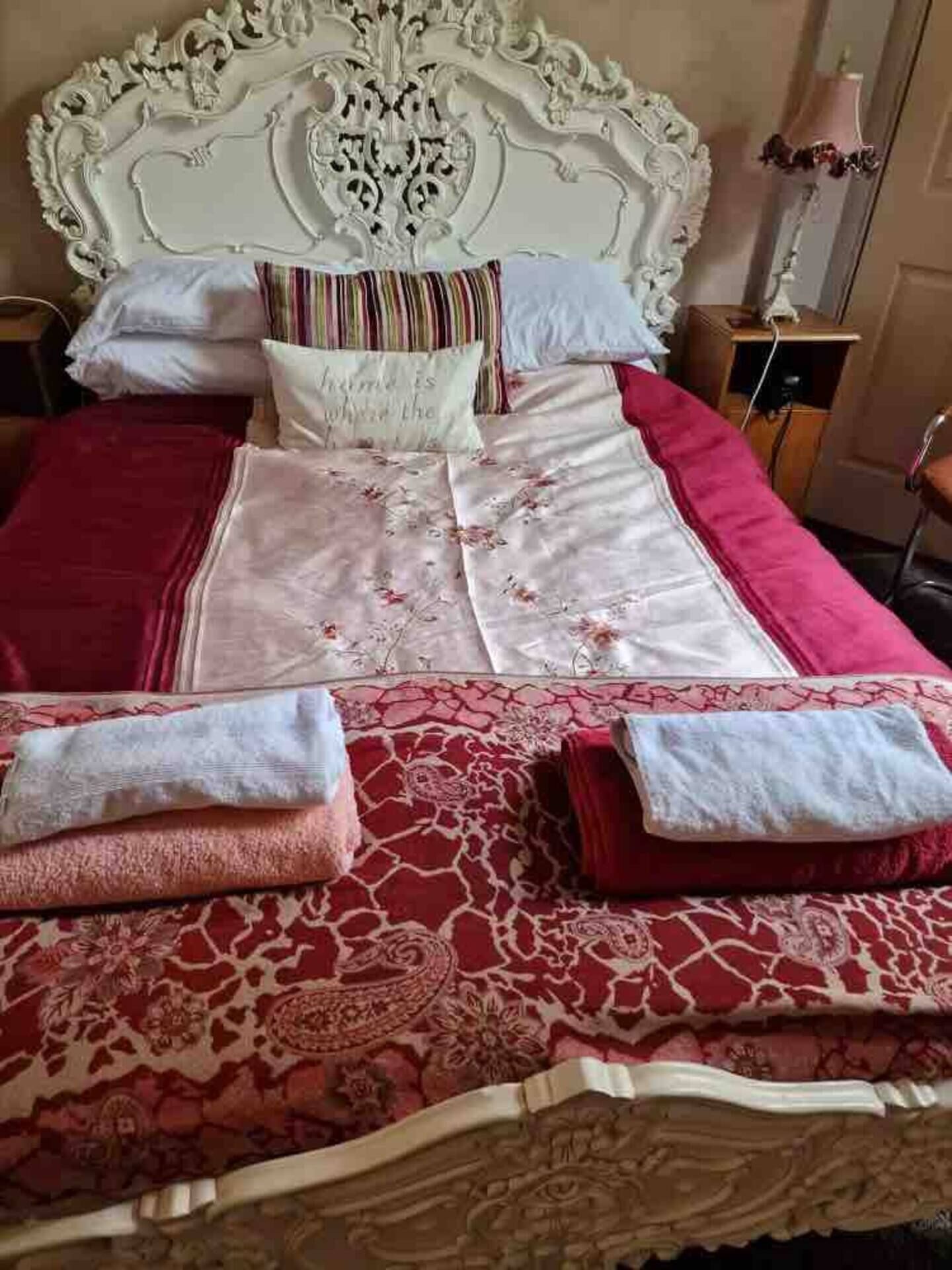 Un lit doté d’une tête de lit blanche ornée, de draps à motifs floraux et de deux serviettes pliées avec soin.