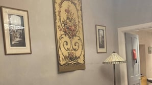Un saló amb un sofà marró fosc, coixins florals, un gran tapís decoratiu i quadres amb marc a les parets.