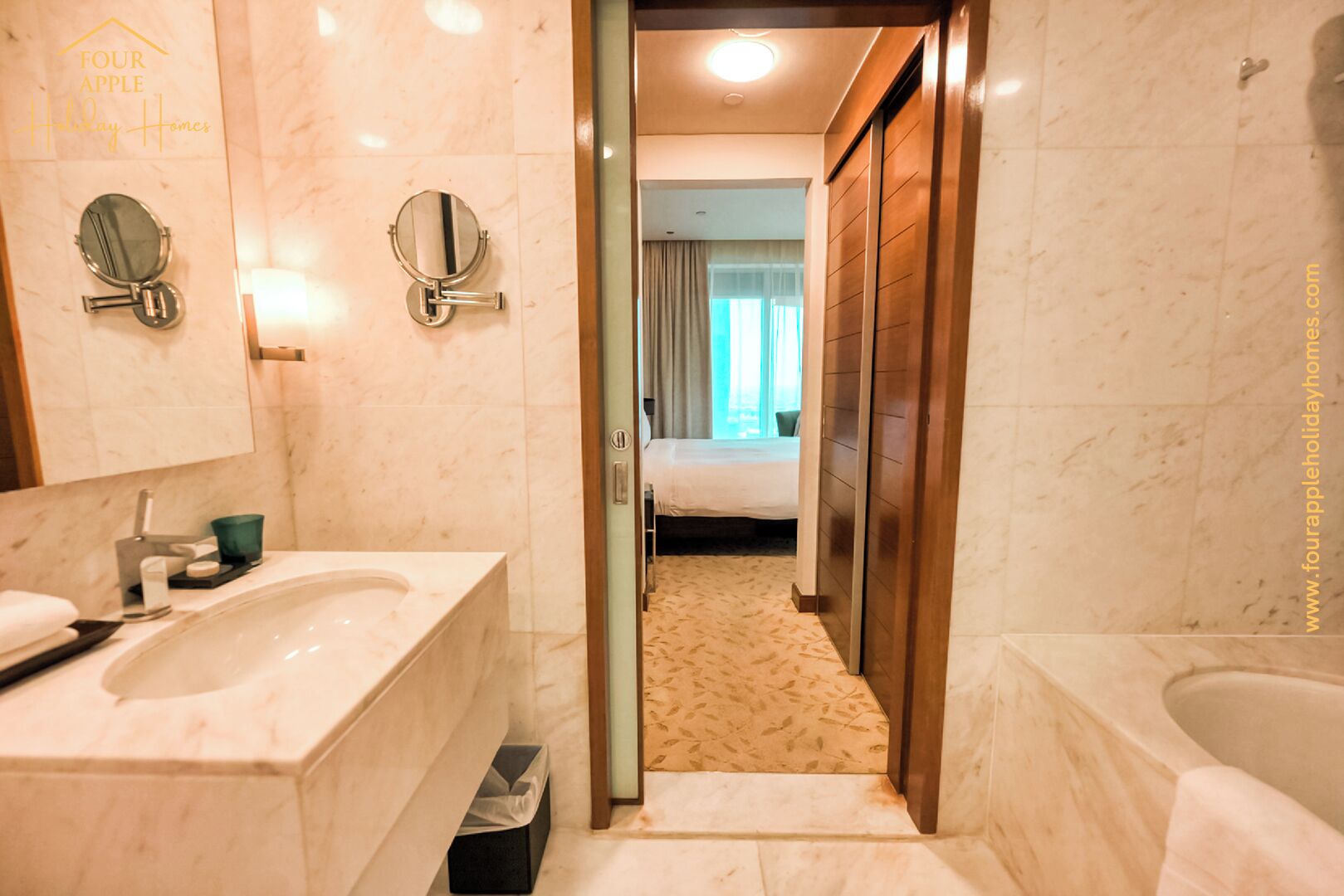 A hotel bathroom with a marble sink, a mirror, and a wooden door leading to a bedroom.