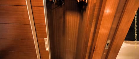 A wooden closet with hanging clothes and a pair of shoes on the floor.