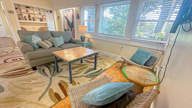A cozy living room with a sofa, a wooden coffee table, a wicker chair, and a patterned rug. - Central Location  Beach Access BBQ  Patio Cottage (Long Beach)