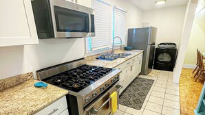 A kitchen with white cabinets, a stainless steel stove, a microwave, and a refrigerator. - Central Location  Beach Access BBQ  Patio Cottage (Long Beach)
