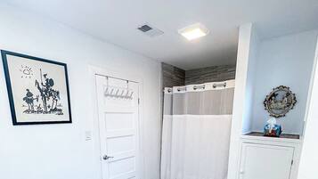 Un baño con una puerta blanca, cortina de ducha, una alfombra pequeña y un cuadro en la pared.