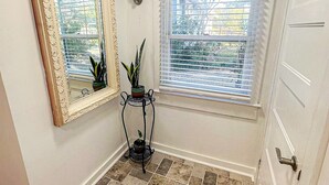 A small, well-lit room with a tiled floor, a large mirror, a window with blinds, and a door with a handle. - Central Location  Beach Access BBQ  Patio Cottage (Long Beach)