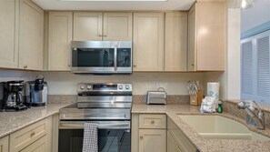 Una cocina moderna con electrodomésticos de acero inoxidable, incluyendo un microondas, horno y tostadora. Hay un lavabo con grifo y una encimera con cafetera y un bloque para cuchillos.
