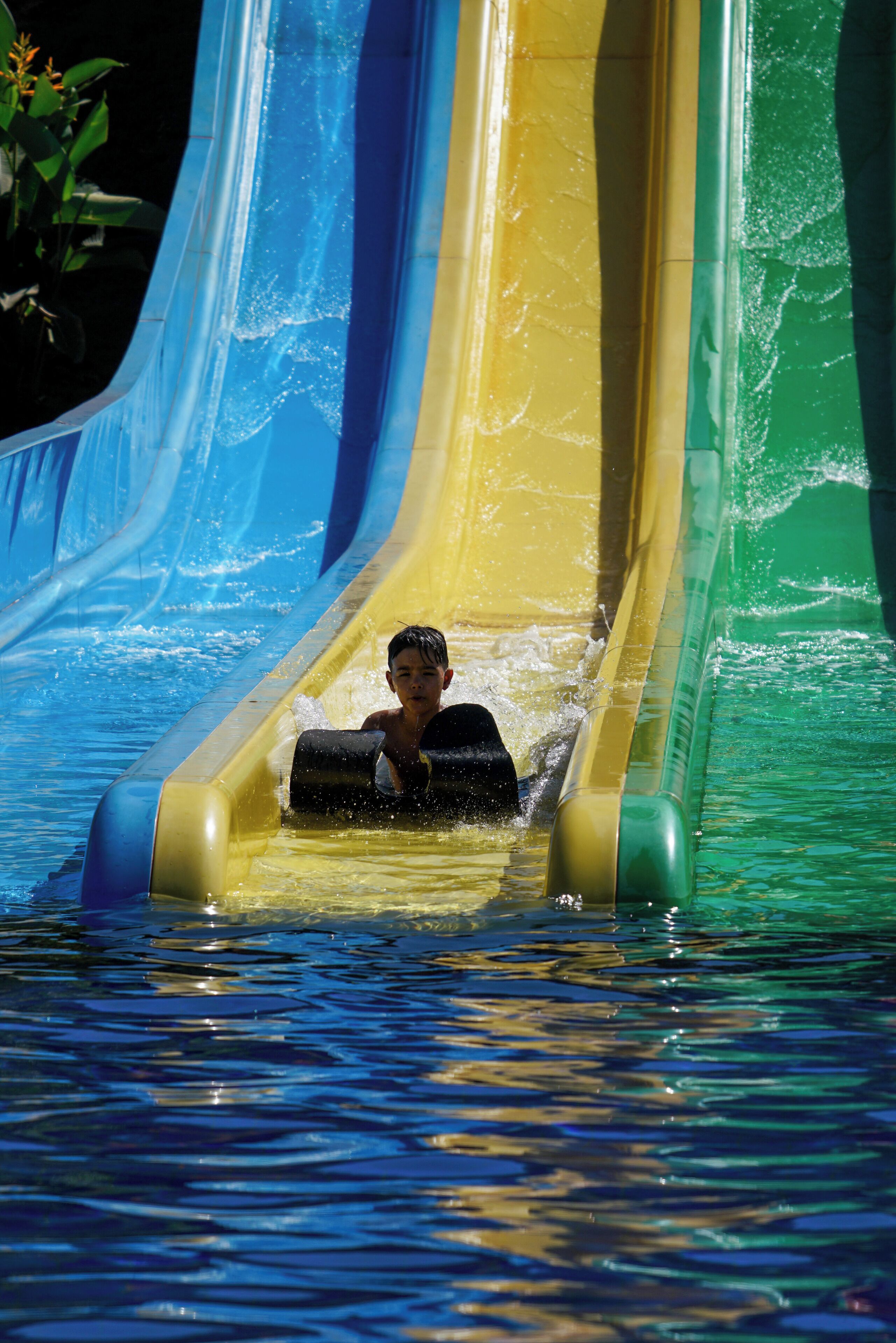 A person sliding down a multi-colored water slide with clear water and a pool at the bottom.