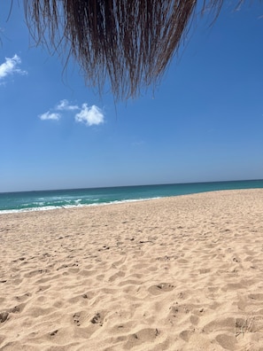 Ein sandiger Strand mit Fußabdrücken und einem strahlend blauen Himmel.