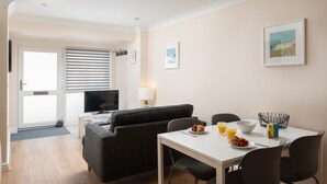 Un salon moderne avec un canapé, une table à manger où sont disposés des aliments pour le petit-déjeuner, un téléviseur et une fenêtre avec des stores.