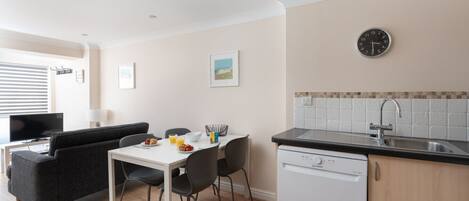 A compact kitchen with a dishwasher, a sink, and a dining area with a table and chairs.