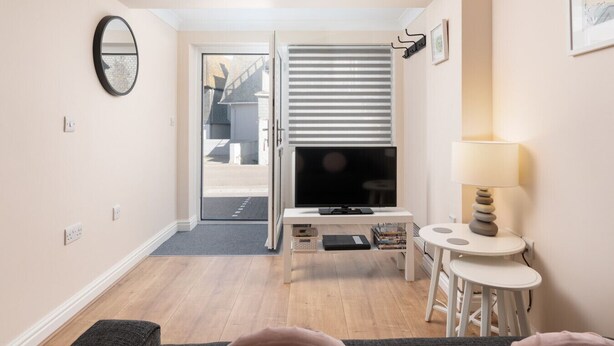 Un espace de vie compact comprenant un téléviseur posé sur un meuble, une petite table avec une lampe et une porte donnant sur un espace extérieur.